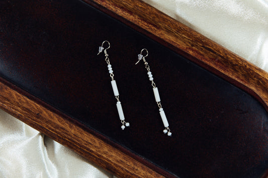 White beaded dangle earrings displayed on a wooden surface