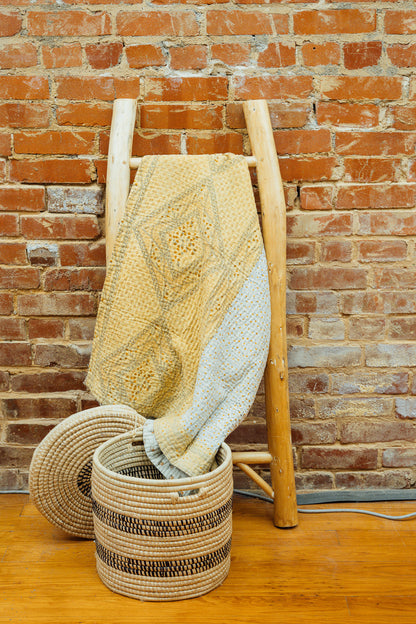 A yellow baby blanket made from quilted kantha material hanging on a blanket ladder.