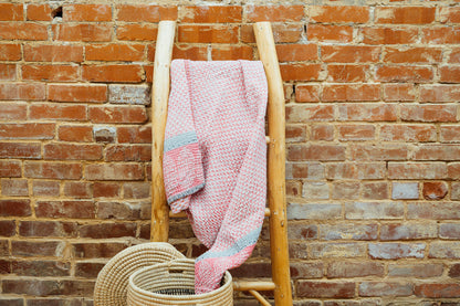 Pink kantha style baby blanket styled on a wooden blanket ladder