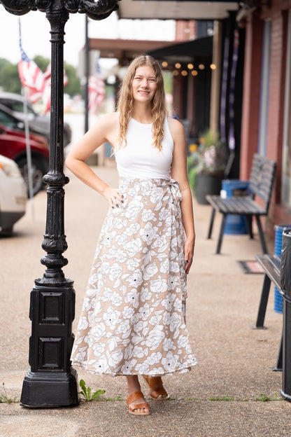 Woman in a white top and floral skirt standing next to a black street lamp on a sidewalk.