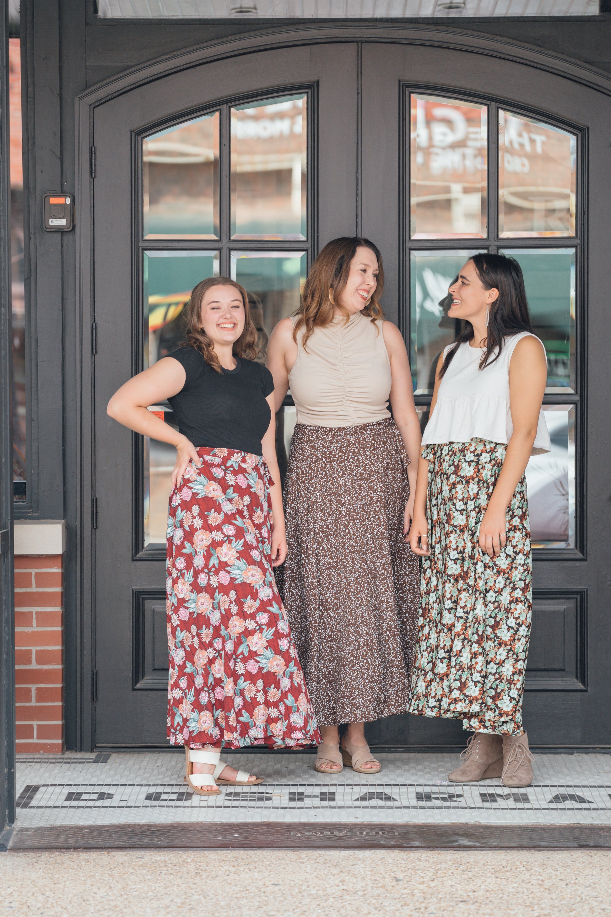 Three women standing side by side, wearing maxi wrap skirts with floral patterns. Each skirt is different colors and patterns.