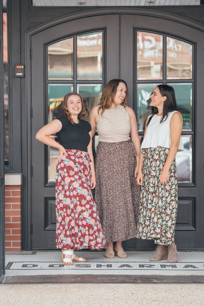 Three women standing side by side, wearing maxi wrap skirts with floral patterns. Each skirt is different colors and patterns.