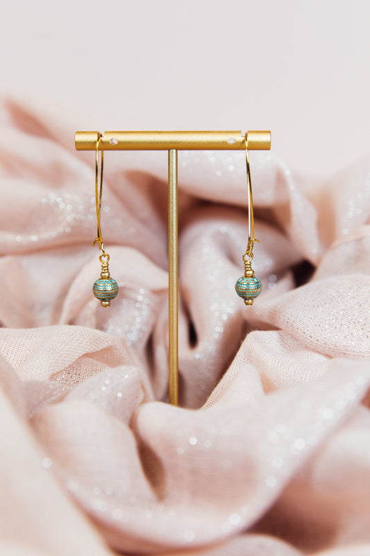 A pair of earrings with gold finished hoops and sea green metal beads, displayed on a pink fabric.