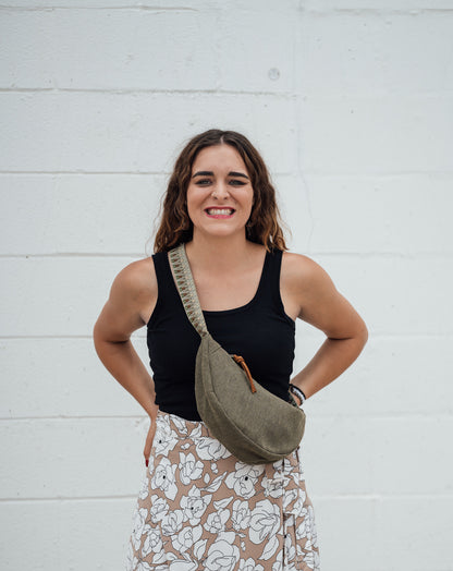 Woman wearing a black tank top and floral skirt with a green Thai Dumpling Sling Bag over her shoulder against a white wall.