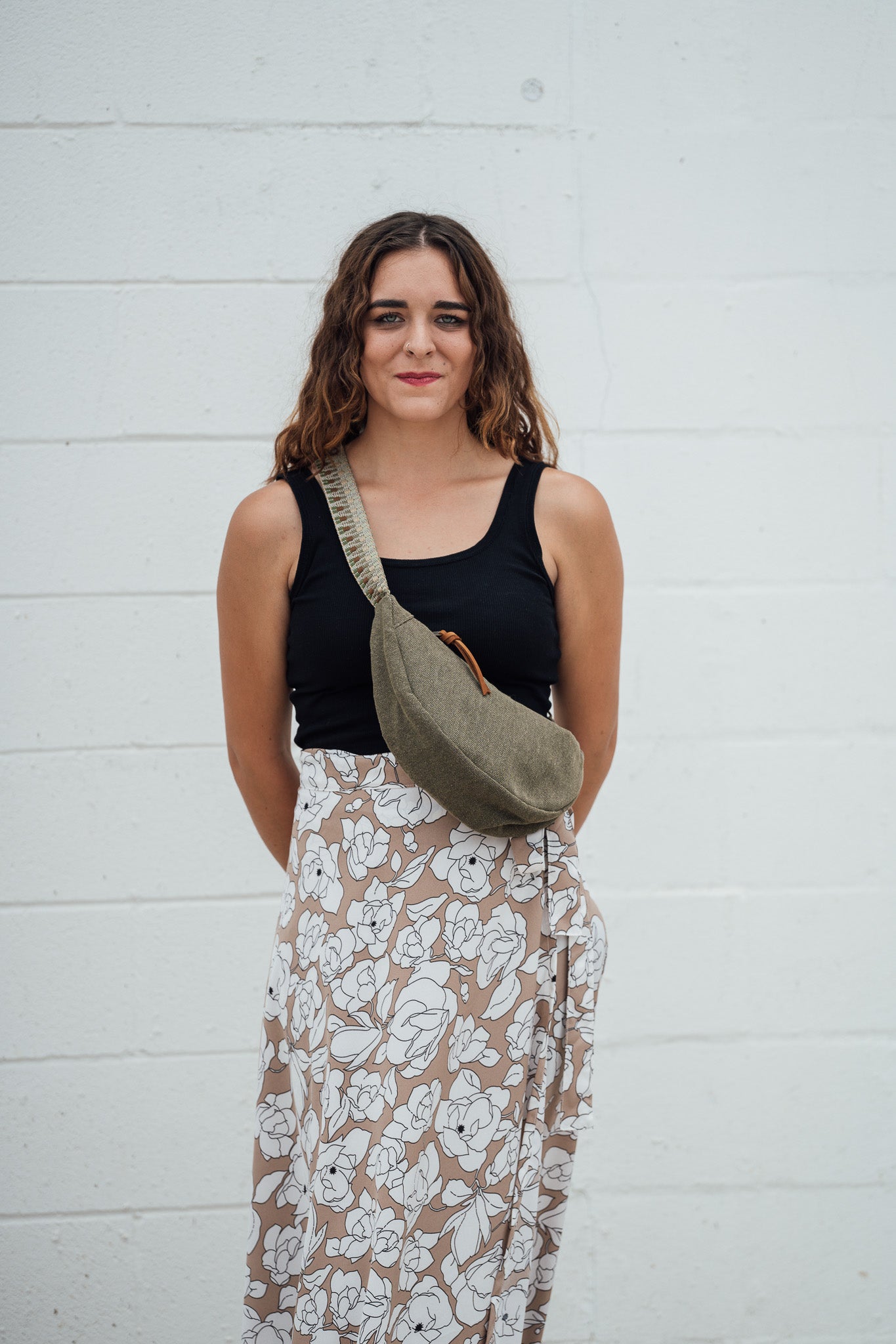 Woman wearing a black top and floral skirt with a green Thai Dumpling Sling Bag against a white wall