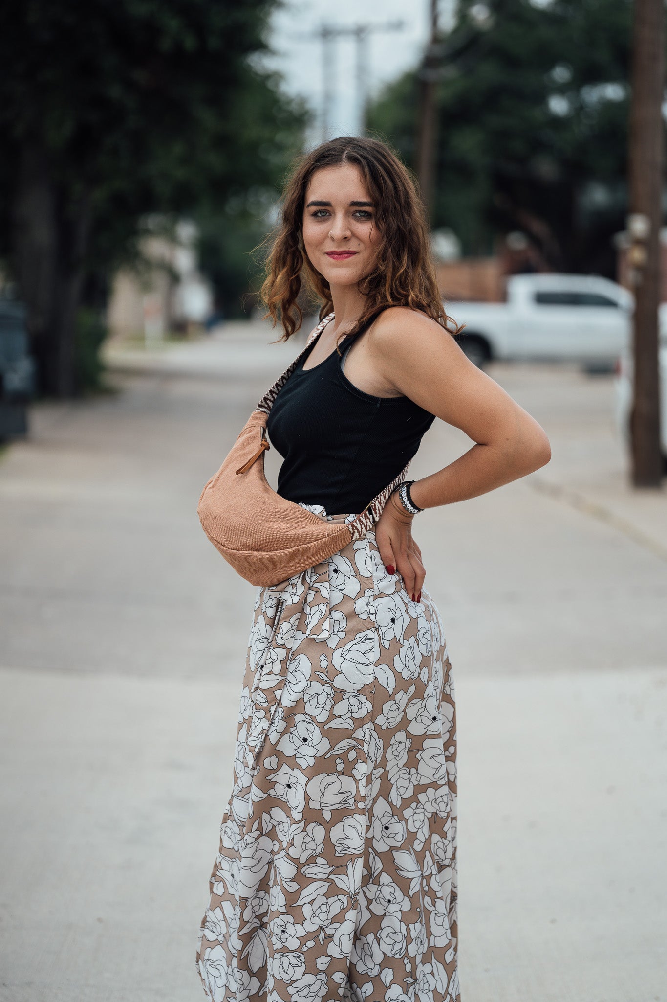 Woman in black tank top and floral skirt holding a Sienna Thai Dumpling Sling Bag on a street.