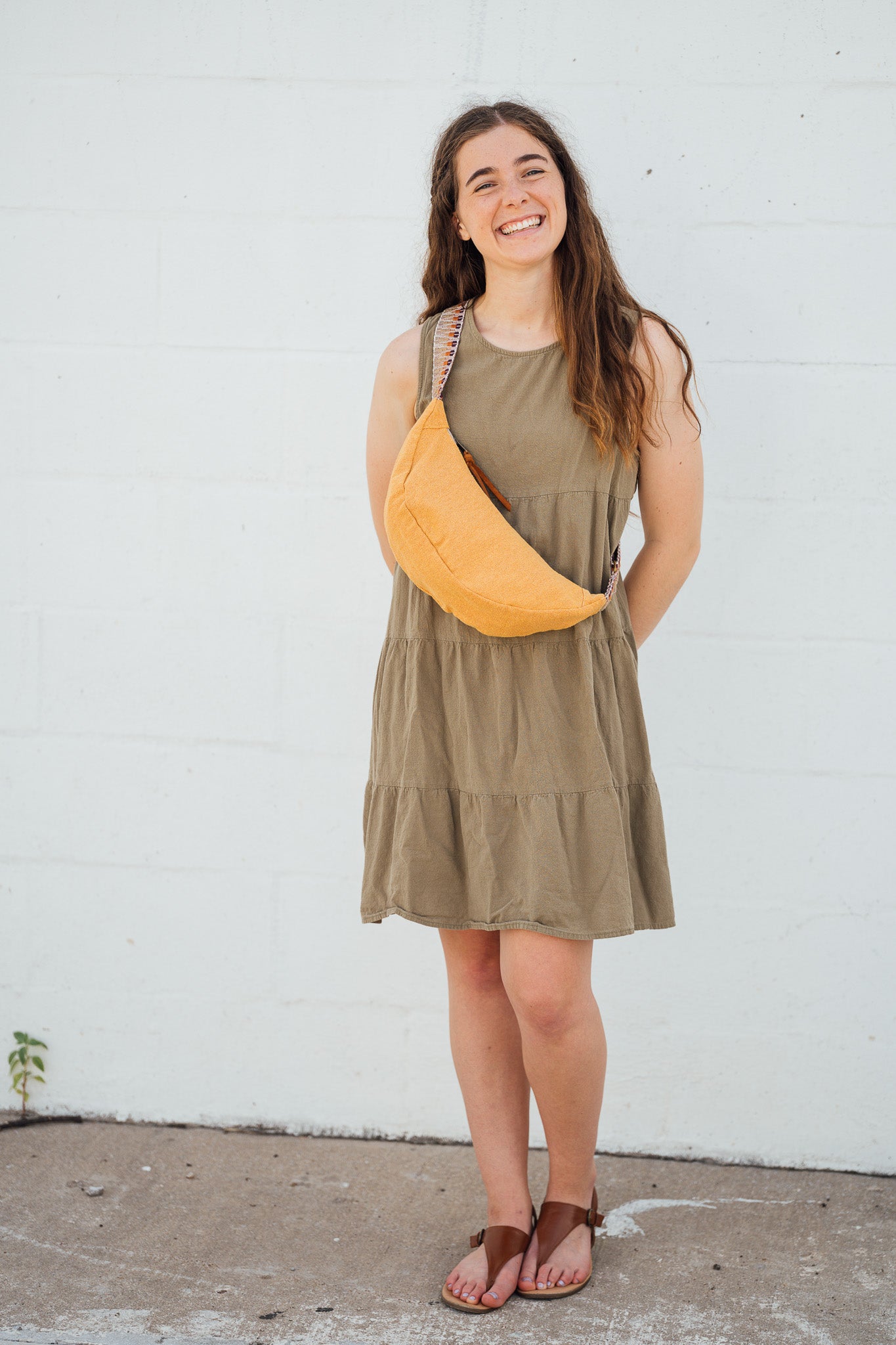 Woman wearing a green dress with a yellow Thai Dumpling Sling Bag against a white wall
