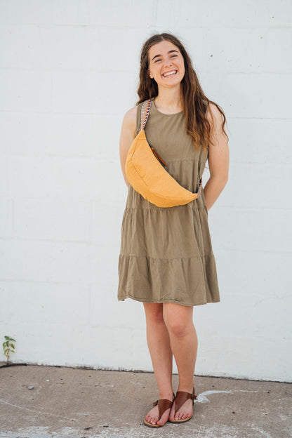 Woman wearing a green dress with a yellow Thai Dumpling Sling Bag against a white wall