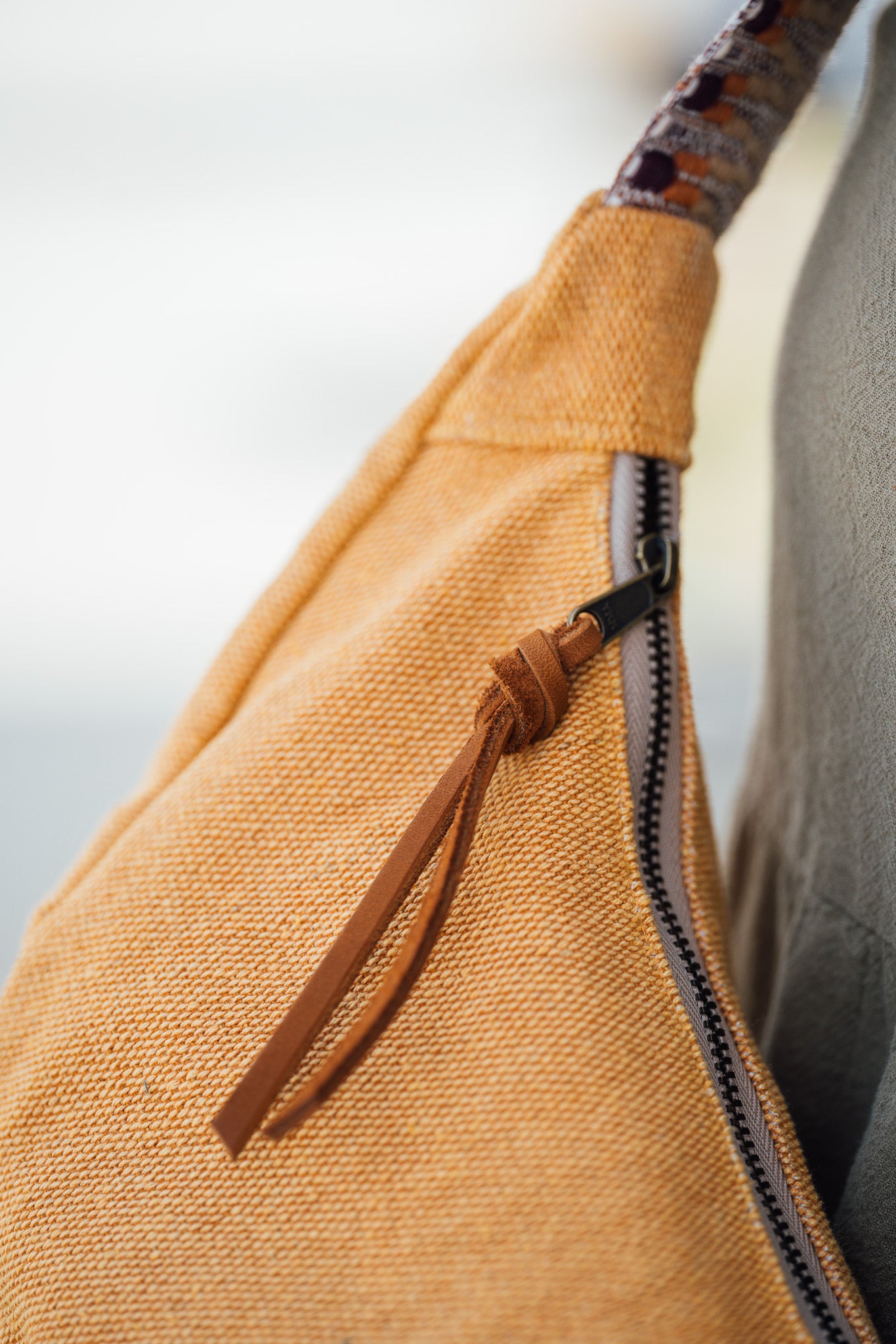Close-up of a thai yellow dumpling bag with a zipper and woven strap against a blurred background