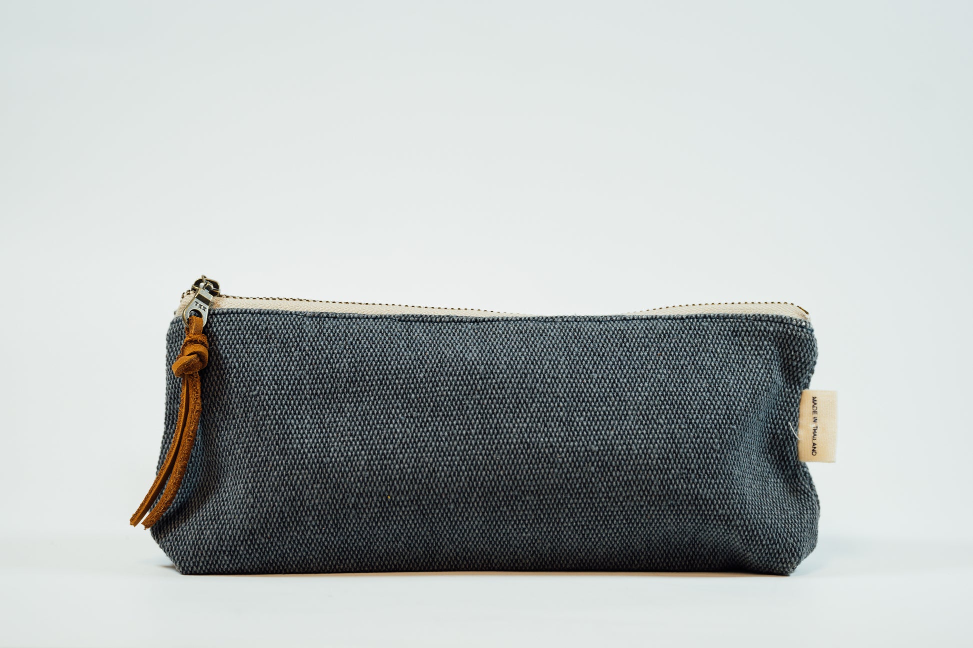 A navy fabric pencil case with a metal zipper and a leather tassel, against a white background.