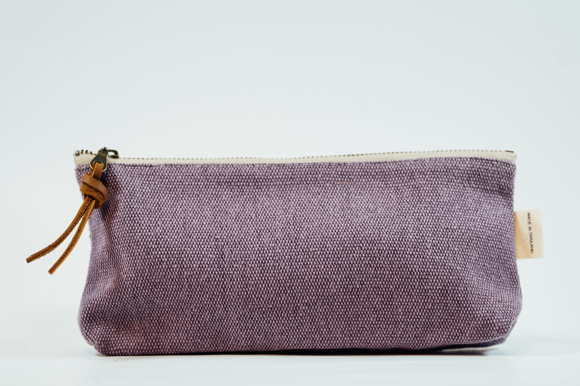 A purple fabric pencil case with a metal zipper and a leather tassel, against a white background.