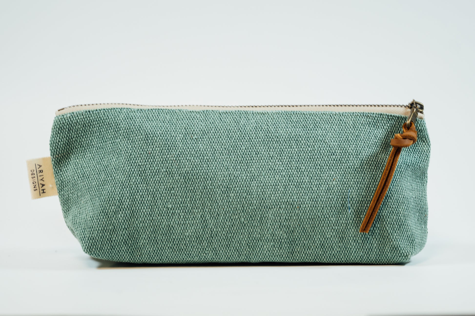 A teal fabric pencil case with a metal zipper and a leather tassel, against a white background.